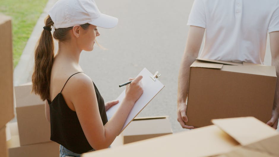 Inside the back of a van loaded with several sealed cardboard moving boxes, some stacked and others placed individually, with the open tailgate providing a view of a suburban street during sunset. The